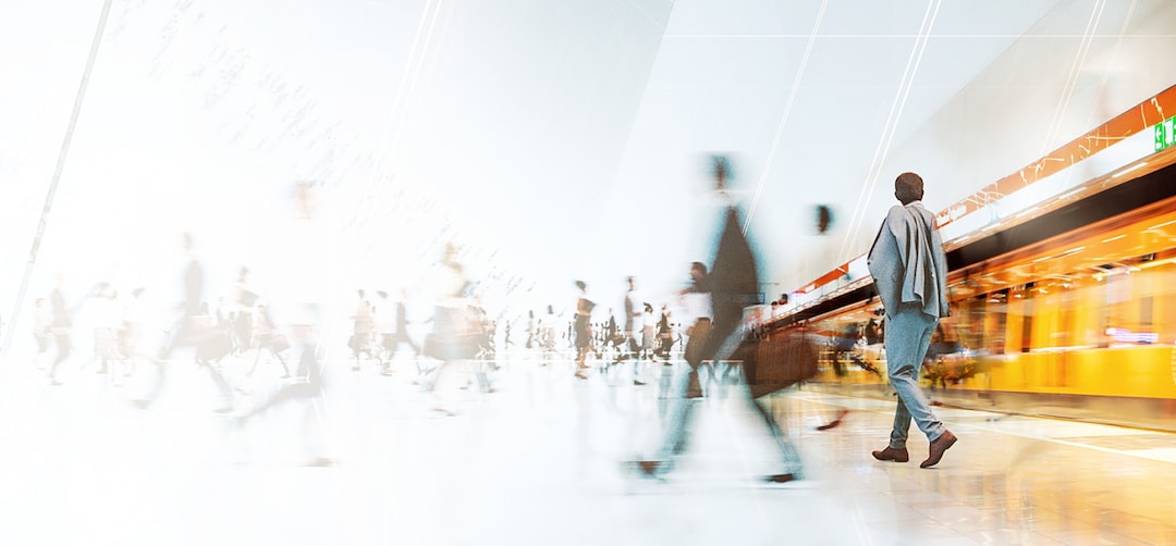Commuters walking through a modern train station with a bright, spacious interior and a sign displaying directions and a clock.